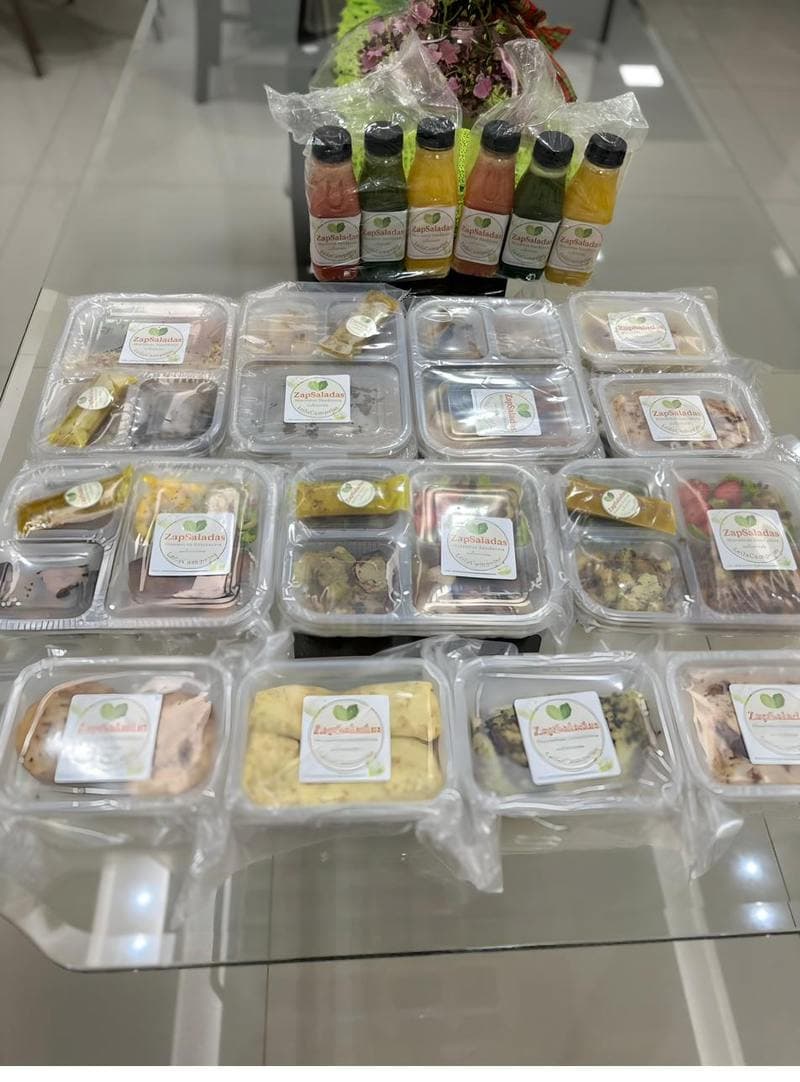 Mesa de produção com marmitas montadas e sucos funcionais da ZapSalada